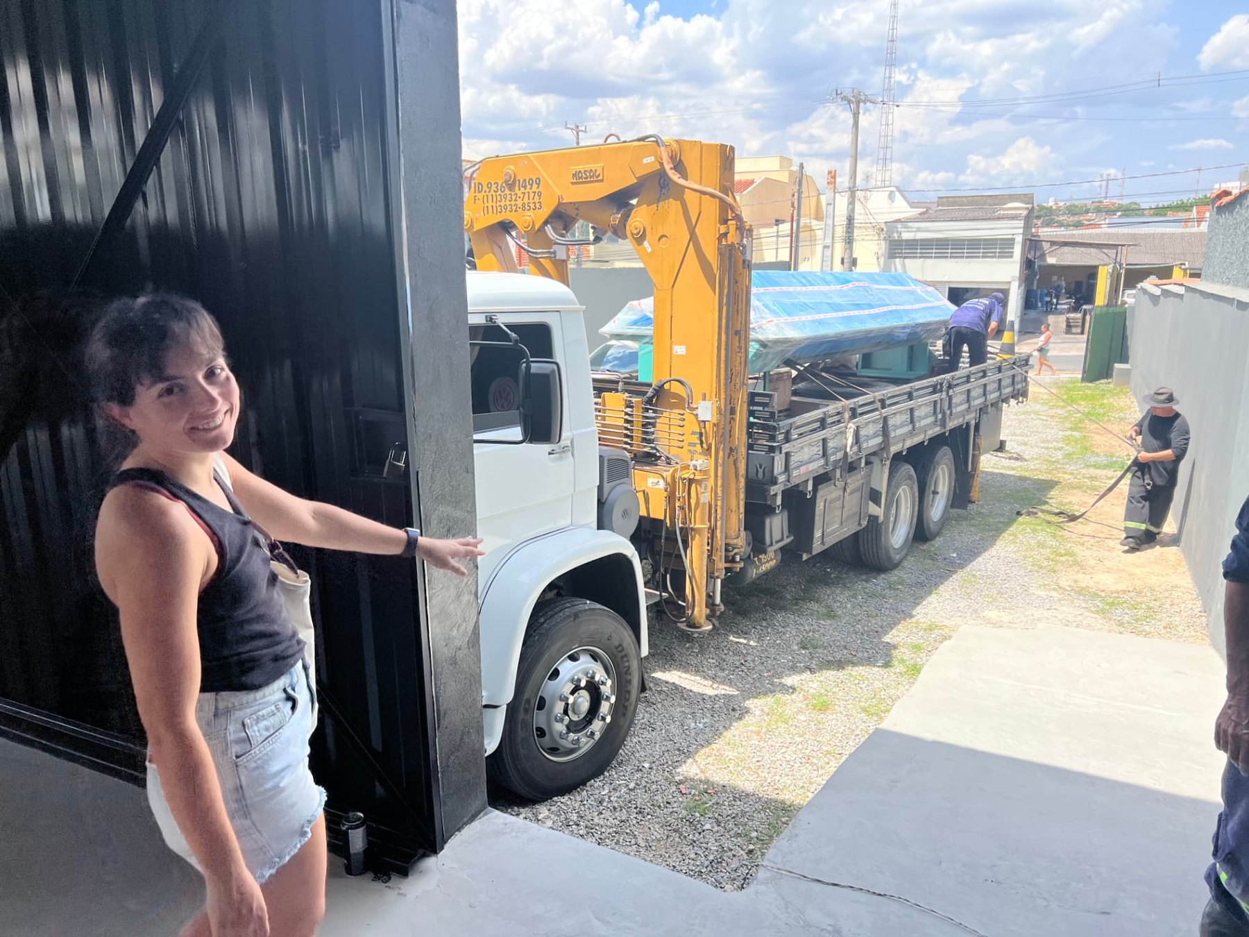 Camila at the factory entrance while the crane truck delivers the wrapped machine
