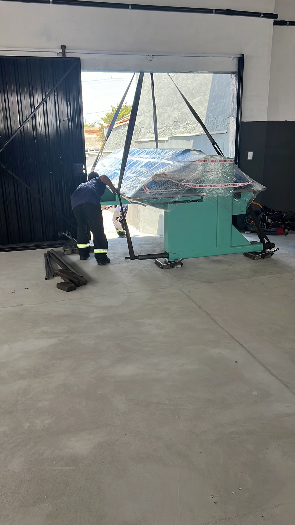 The wrapped green machine suspended from lifting straps inside the factory